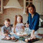 Dzieci i mama dekorują truskawkowe desery z kremem w jasnej kuchni