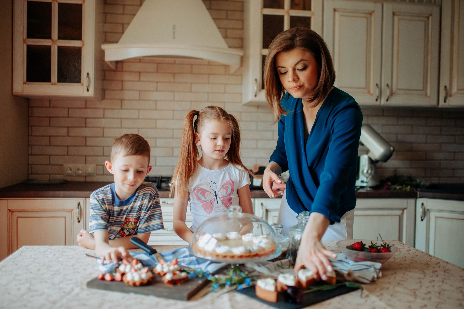 Dzieci i mama dekorują truskawkowe desery z kremem w jasnej kuchni